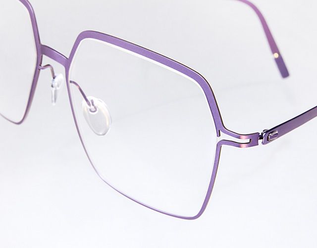 Close-up of Titanium Reframed eyeglasses showing the laser-cut titanium full-rim frame, flat sculpted profile, and minimalist snap hinge in a vibrant purple finish.