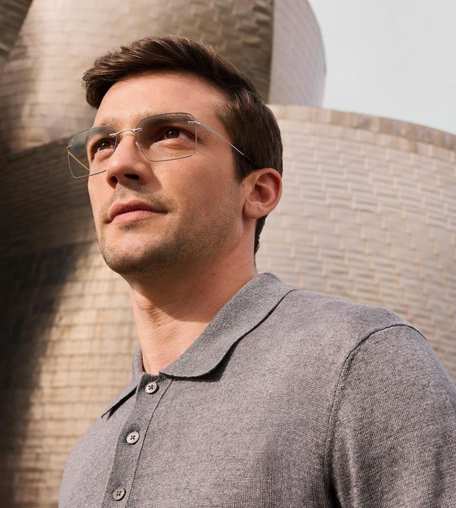Man wearing a grey polo shirt and silver rimless glasses with grey Color Groove on the lens edges, standing in front of the Guggenheim Bilbao Museum