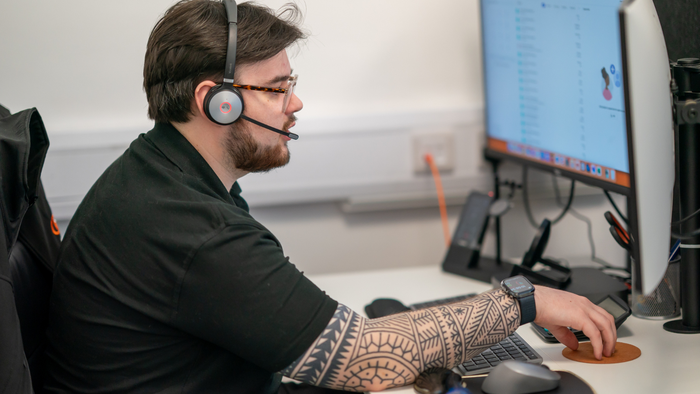 A person with a headset and tattooed arm works at a computer, using a mouse.