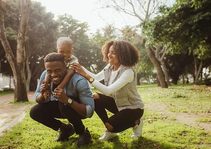 A father, mother, and young son smiling and playing in a park