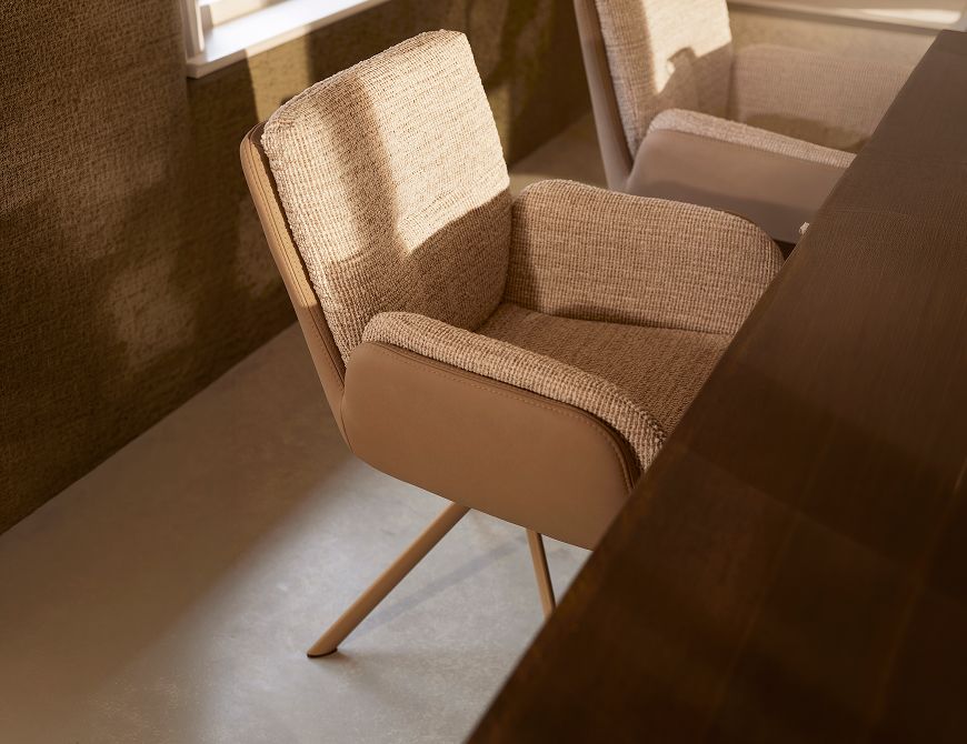 A modern beige armchair with fabric upholstery and wooden legs is positioned beside a dark wooden table in a softly lit room.