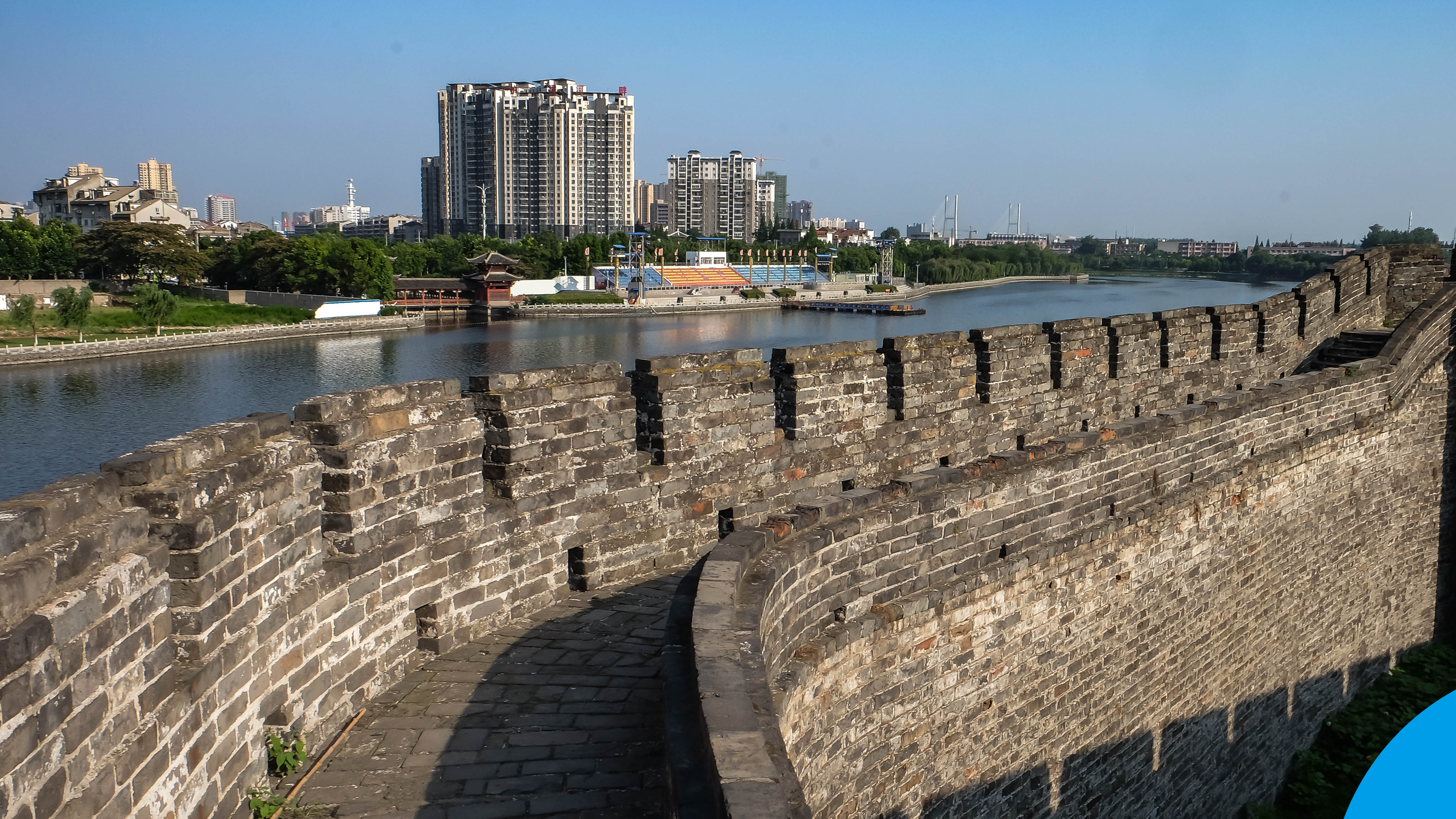 Ancient city wall overlooking a river with modern high rise buildings and a clear blue sky in Jingzhou, China.