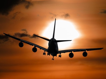 Silhouette of a large airplane flying against a dramatic orange sunset sky, with the sun glowing behind the aircraft.